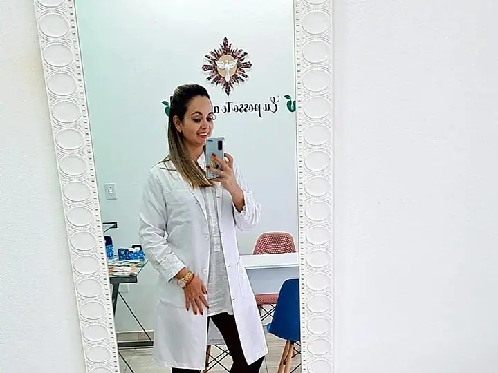 Natacha Ludkiewicz de jaleco branco, refletida no espelho do consultório
