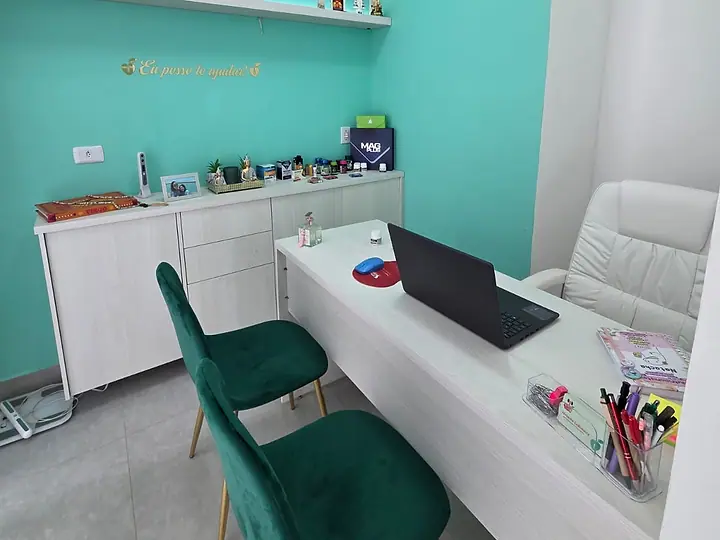 Sala de atendimento com mesa branca, cadeiras verdes e parede verde-água